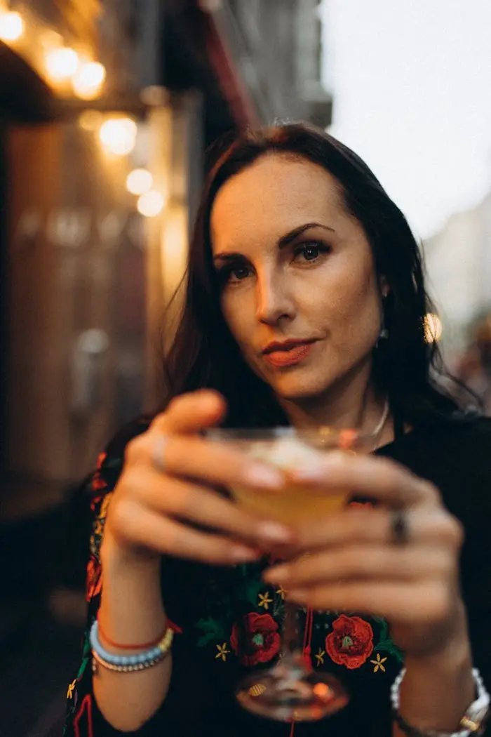 Elegant brunette woman in Lviv, Ukraine, enjoying a refreshing drink at an outdoor setting during the evening.